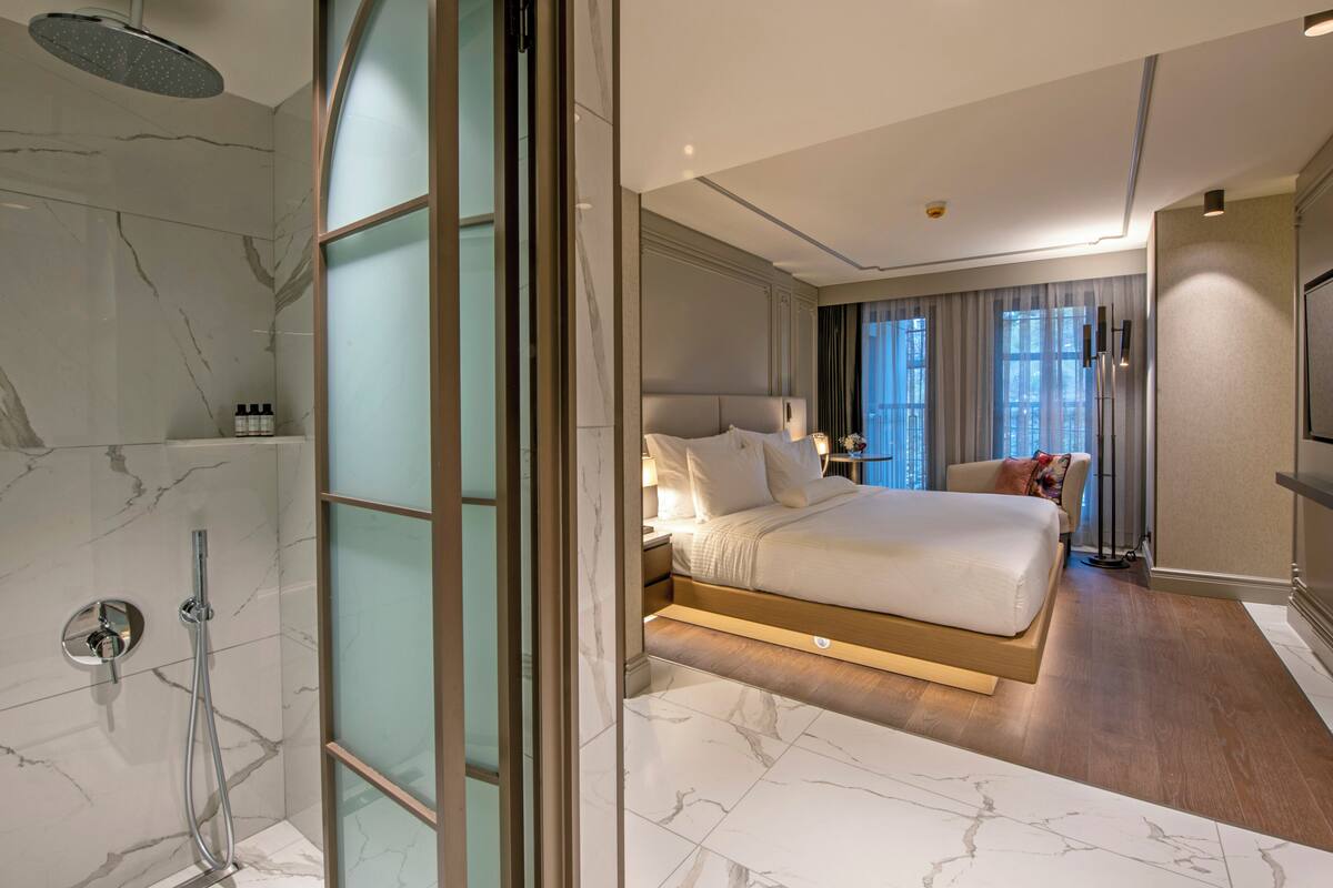 A modern hotel room with a marble bathroom, a large bed, a TV, and a view of the city.