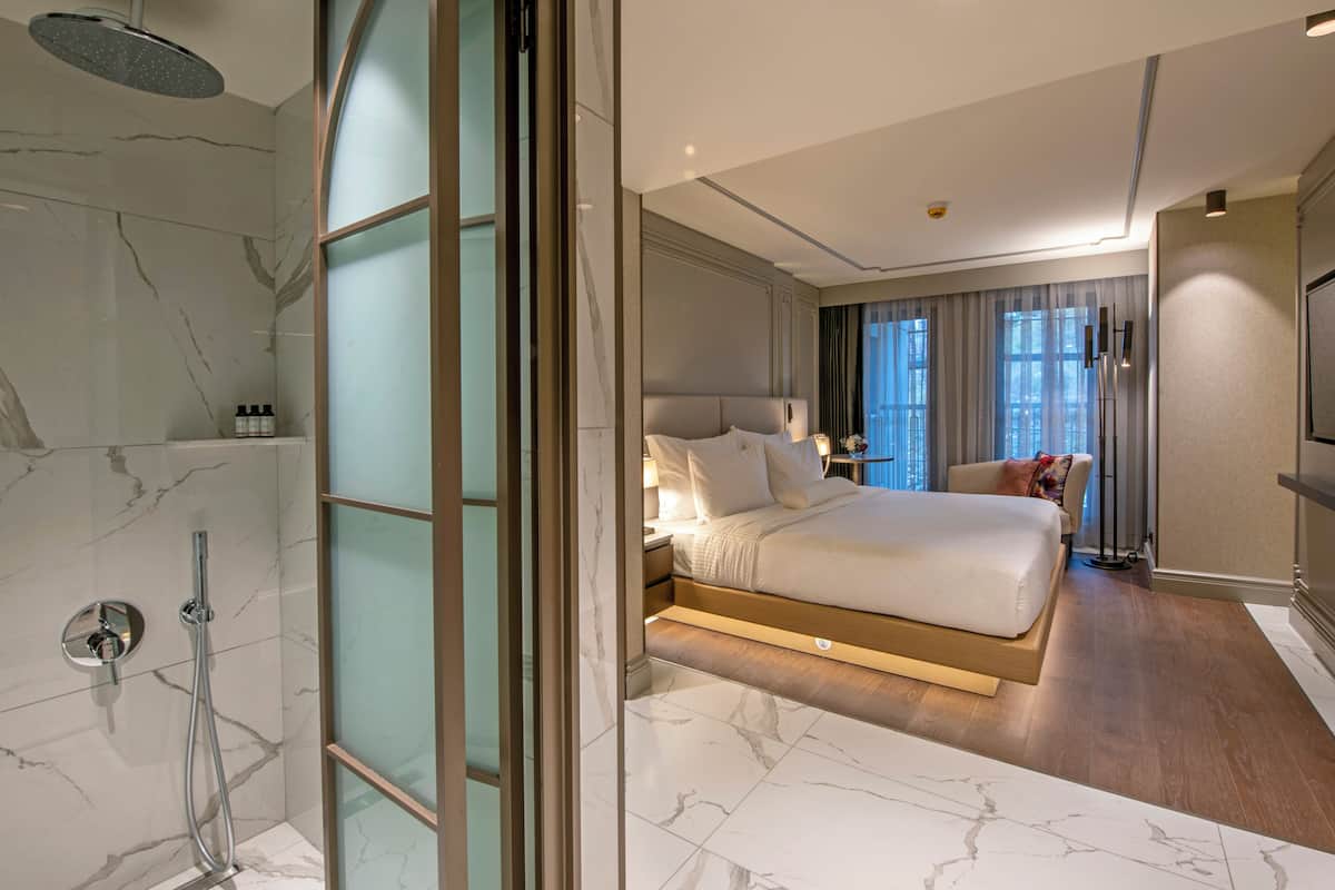 Ein modernes Hotelzimmer mit Marmorbadezimmer, einem großen Bett, einem Fernseher und Blick auf die Stadt.