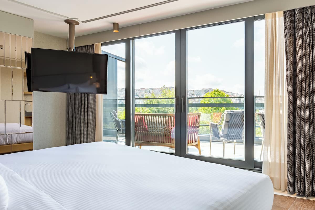 Ein Hotelzimmer mit einem großen Bett, einem an der Wand montierten Fernseher und einem Balkon mit Sitzgelegenheit.