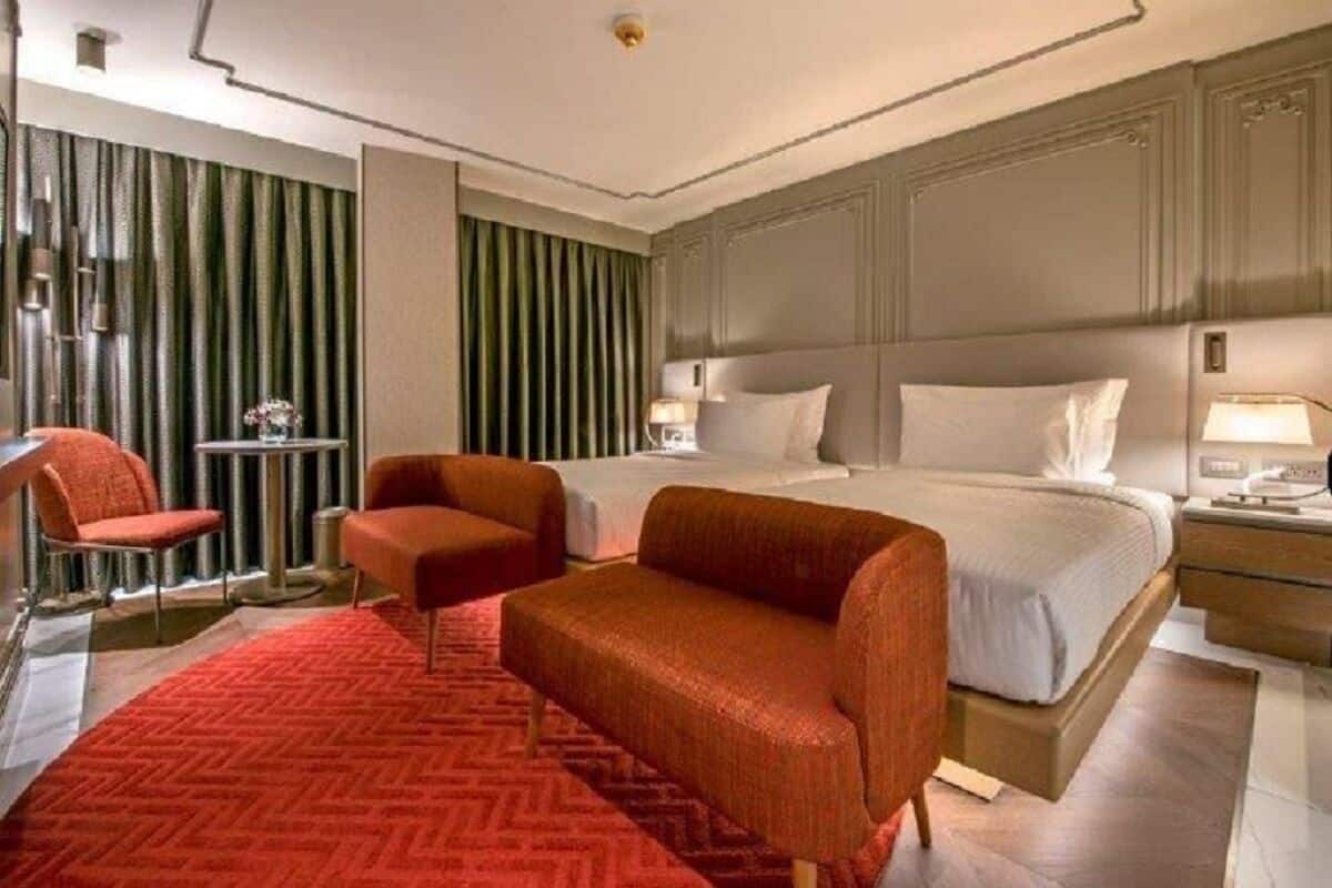 A hotel room with a bed, two armchairs, a small table, and a red carpet.