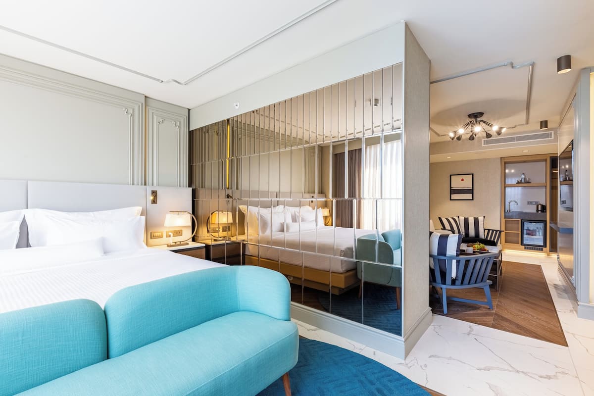 A hotel room with a large bed, a seating area with a blue sofa, a small table, and a view of the hallway.