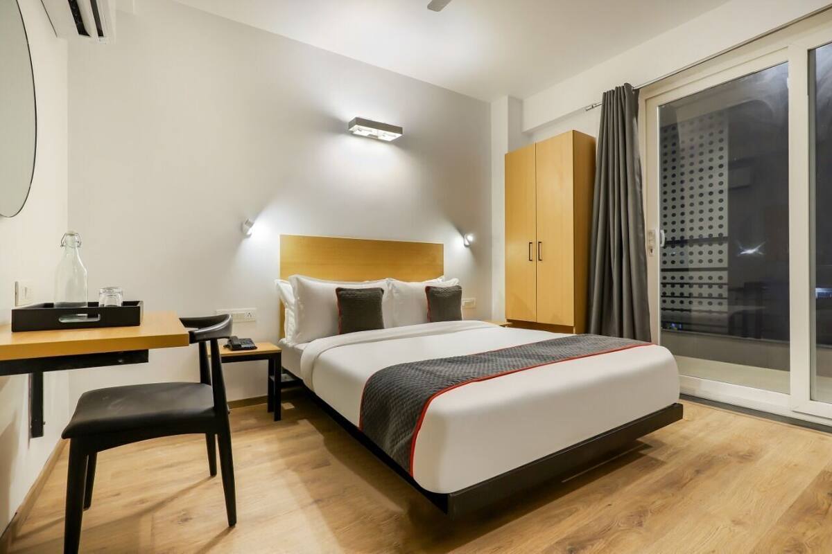 A hotel room with a bed, a desk, a chair, a wardrobe, and a sliding glass door.