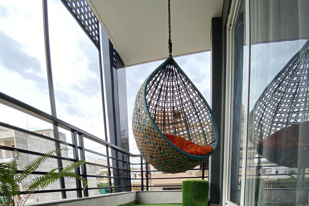 A balcony with artificial grass, a hanging chair, and a potted plant.