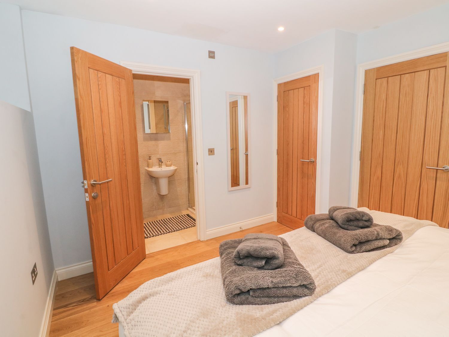A bedroom with two wooden doors, a large bed with white bedding, and two towels on the bed.
