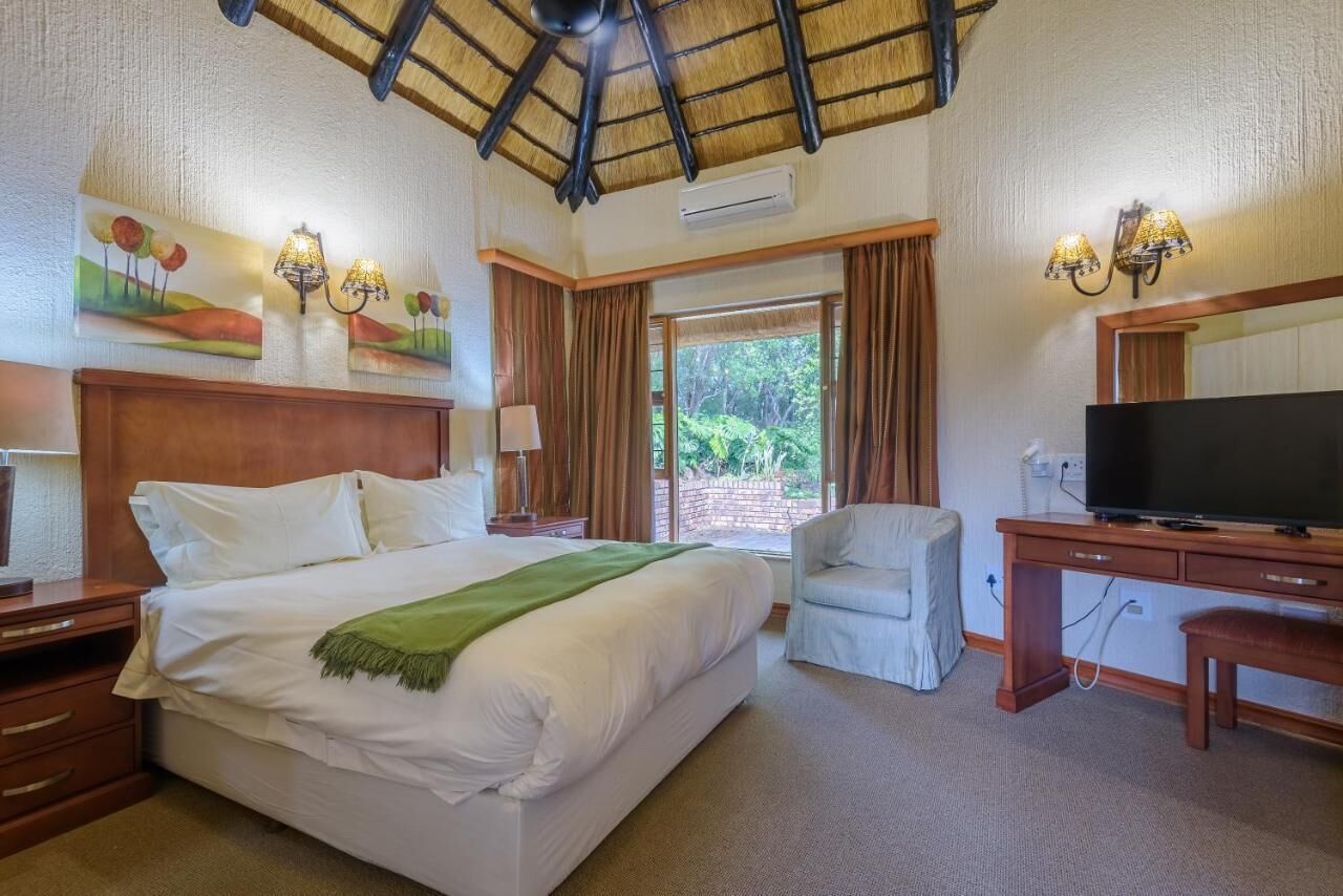 A hotel room with a large bed, a desk with a television, a chair, and artwork on the walls.