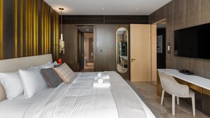 A modern hotel room with a large bed, a desk, a chair, a TV, and a mirror.