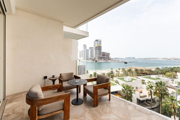 Un balcón con vista al mar y al paisaje urbano, amoblado con sillas y una mesa de madera.