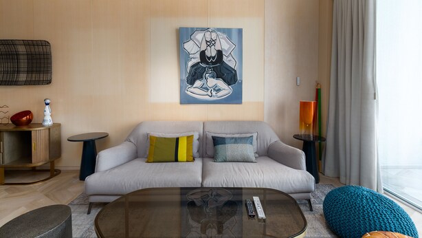 A modern living room with a grey sofa, a glass coffee table, and a painting on the wall.