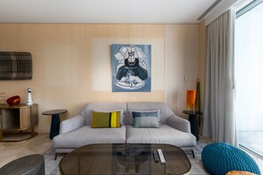 A modern living room with a grey sofa, a glass coffee table, and a painting on the wall.