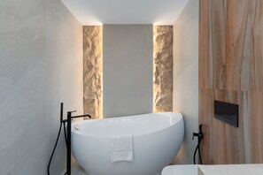 Un baño moderno con una bañera independiente, paredes de mármol y un panel decorativo de madera.