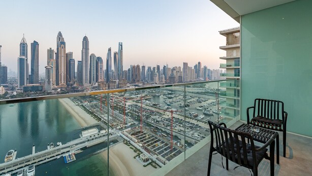 A high-rise balcony with a city view, two chairs, and a glass railing.