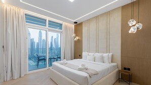 A modern hotel room with a large bed, a view of a cityscape, and a balcony with a chair.