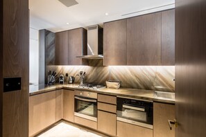 A modern kitchen with wooden cabinetry, stainless steel appliances, and a marble backsplash.