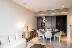 A modern dining area with a round table, white upholstered chairs, and a light-colored sofa.