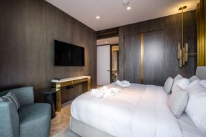 Una habitación de hotel moderna con una cama grande, un televisor de pantalla plana montado en la pared, un escritorio pequeño con una silla y un vestidor.