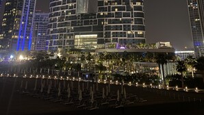 Een hoog hotel met een opvallende, gebogen gevel, meerdere balkons en een goed verlicht entreegebied met palmbomen en terrasmeubels.