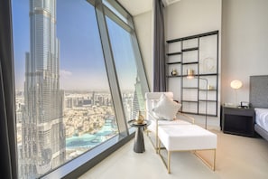 A modern bedroom with a large window offering a cityscape view, a white sofa, a bedside table with a lamp, and a black shelving unit.