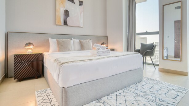 A modern hotel room with a large bed, a bedside table with a lamp, a chair, and a view of the outdoors. - Contemporary Apt with Burj Khalifa View (Dubai)