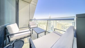 A balcony with a sofa, armchair, and table, overlooking a cityscape with modern buildings. - Contemporary Apt with Burj Khalifa View (Dubai)