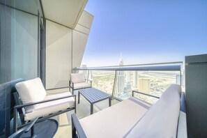 Ein Balkon mit einer Couch, einem Sessel und einem Tisch mit Blick auf eine Stadtlandschaft und moderne Gebäude.