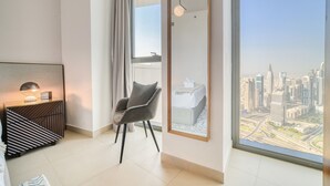 A modern hotel room with a large window offering a city view, a comfortable chair, a bedside table with a lamp, and a framed artwork on the wall. - Contemporary Apt with Burj Khalifa View (Dubai)