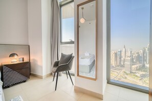 Une chambre d’hôtel moderne dotée d’une grande fenêtre donnant sur la ville, d’un fauteuil confortable, d’une table de chevet avec une lampe et d’une œuvre d’art encadrée accrochée au mur.