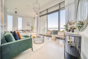 A modern living room with a green sofa, a round coffee table, and a large window offering a city view.