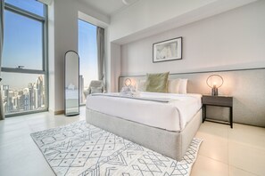 A modern bedroom with a large bed, a city view, a mirror, and a bedside table with a lamp.