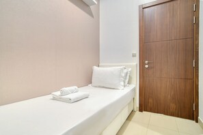 Un petit lit bien fait, avec du linge de lit blanc et des oreillers, une porte en bois et un mur sobre.
