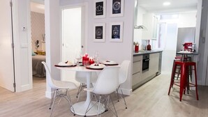 Une cuisine moderne avec des meubles blancs, un tabouret rouge et un coin repas comprenant une table et des chaises blanches.