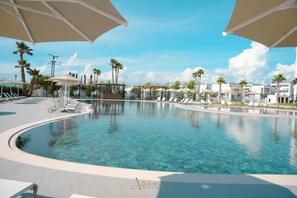 A resort pool area with clear water, lounge chairs, umbrellas, and palm trees. - Adamas Resort & Hotel (Shënkoll)