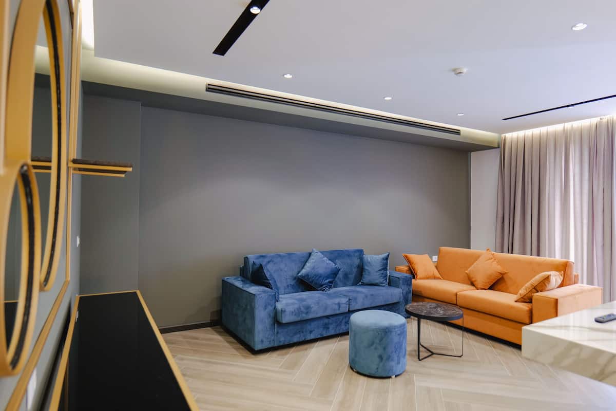 A modern living room with a blue sofa, an orange sofa, and a small round ottoman.