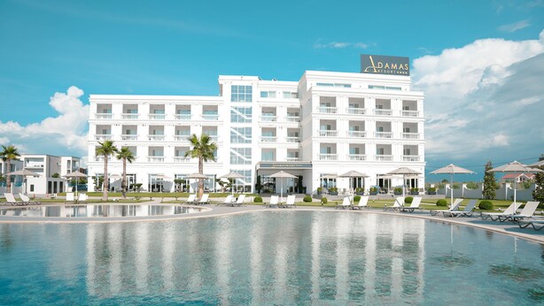 A large hotel with a swimming pool, multiple balconies, and palm trees. - Adamas Resort & Hotel (Shënkoll)