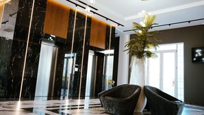 A modern lobby with a marble floor, a large potted plant, and two dark armchairs. - Adamas Resort & Hotel (Shënkoll)