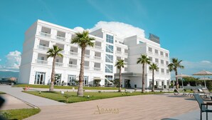 A large white hotel with multiple balconies and palm trees. - Adamas Resort & Hotel (Shënkoll)
