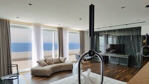 A modern hotel room with a large bed, a seating area, a TV, and a view of the ocean. - Adamas Resort & Hotel (Shënkoll)