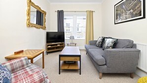 A living room with a grey sofa, a wooden coffee table, a television, a chessboard, and a framed picture on the wall. - Modern Flat on Rose Street (Edinburgh)