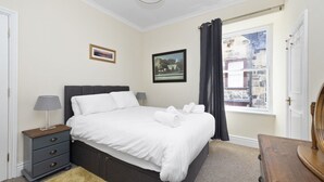A neatly arranged bedroom with a bed, bedside table, lamp, and a window with curtains. - Modern Flat on Rose Street (Edinburgh)