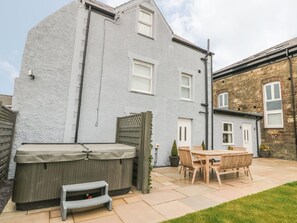 A patio area with a hot tub, wooden table and chairs, and a small step stool. - Fishermans Cottage (Bodorgan)