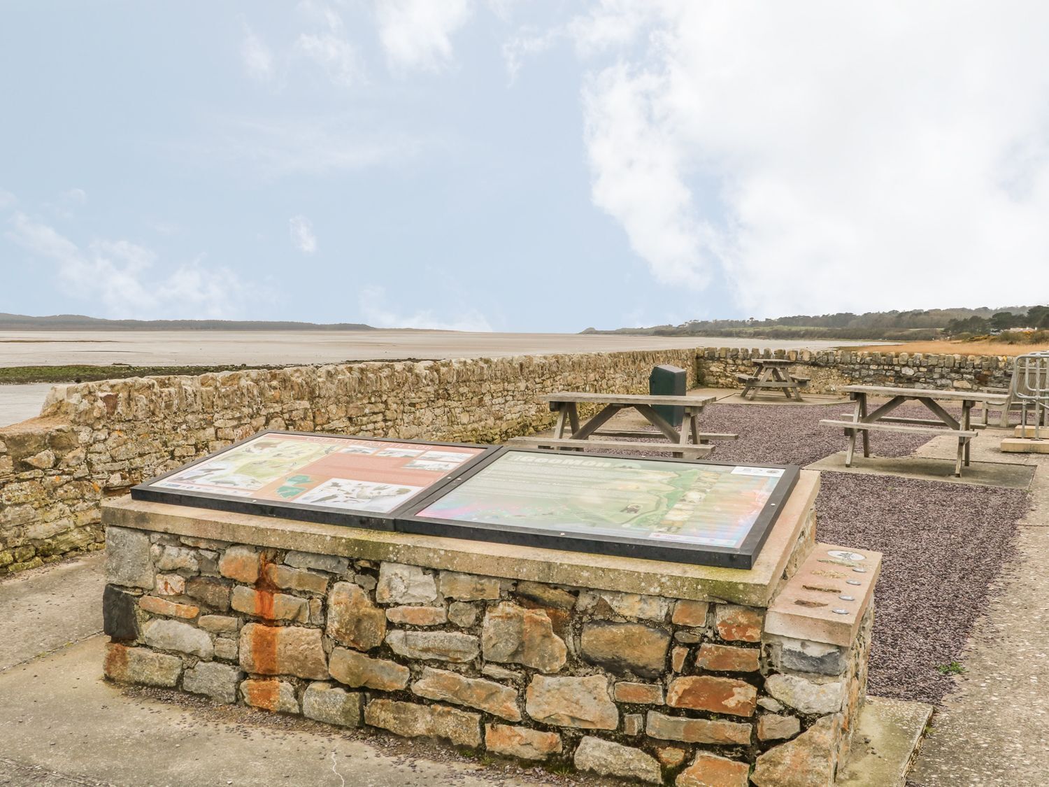 Un mur de pierres sur lequel est affichée une carte et à côté duquel se trouvent des tables de pique-nique.