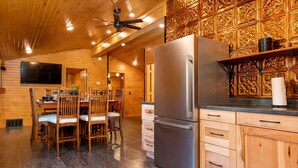 Un intérieur en bois comprenant un grand réfrigérateur, des placards en bois et un coin repas avec des chaises et une table.