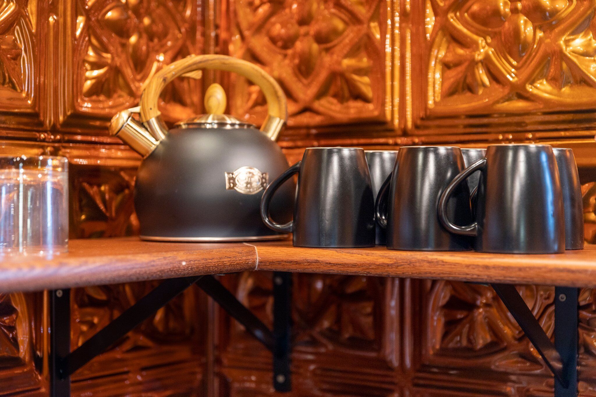 Uma mesa de madeira com uma chaleira preta e quatro xícaras pretas.