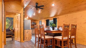 L’intérieur d’un chalet en bois comprend une table à manger, quatre chaises, un ventilateur de plafond et un coin cuisine.