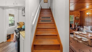A wooden staircase leading to a living area with a fireplace, a dining table, and a sofa.