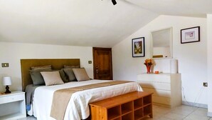 Une chambre à coucher comprenant un lit, une table de chevet, un banc, une commode et un miroir au mur.