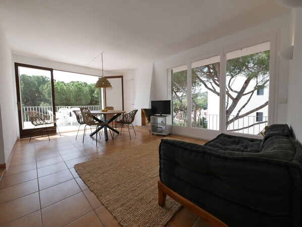 Un vaste espace de vie comprenant un canapé, une table à manger avec des chaises, un téléviseur et un balcon doté d’une balustrade.