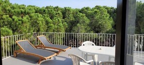 Un balcon doté de deux chaises longues et d’une table, entouré d’une balustrade blanche, et offrant une vue sur une forêt verdoyante et luxuriante.