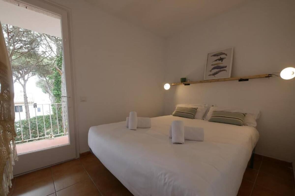 A bedroom with a large bed, a window with a view of trees, and a wall-mounted shelf with a picture.