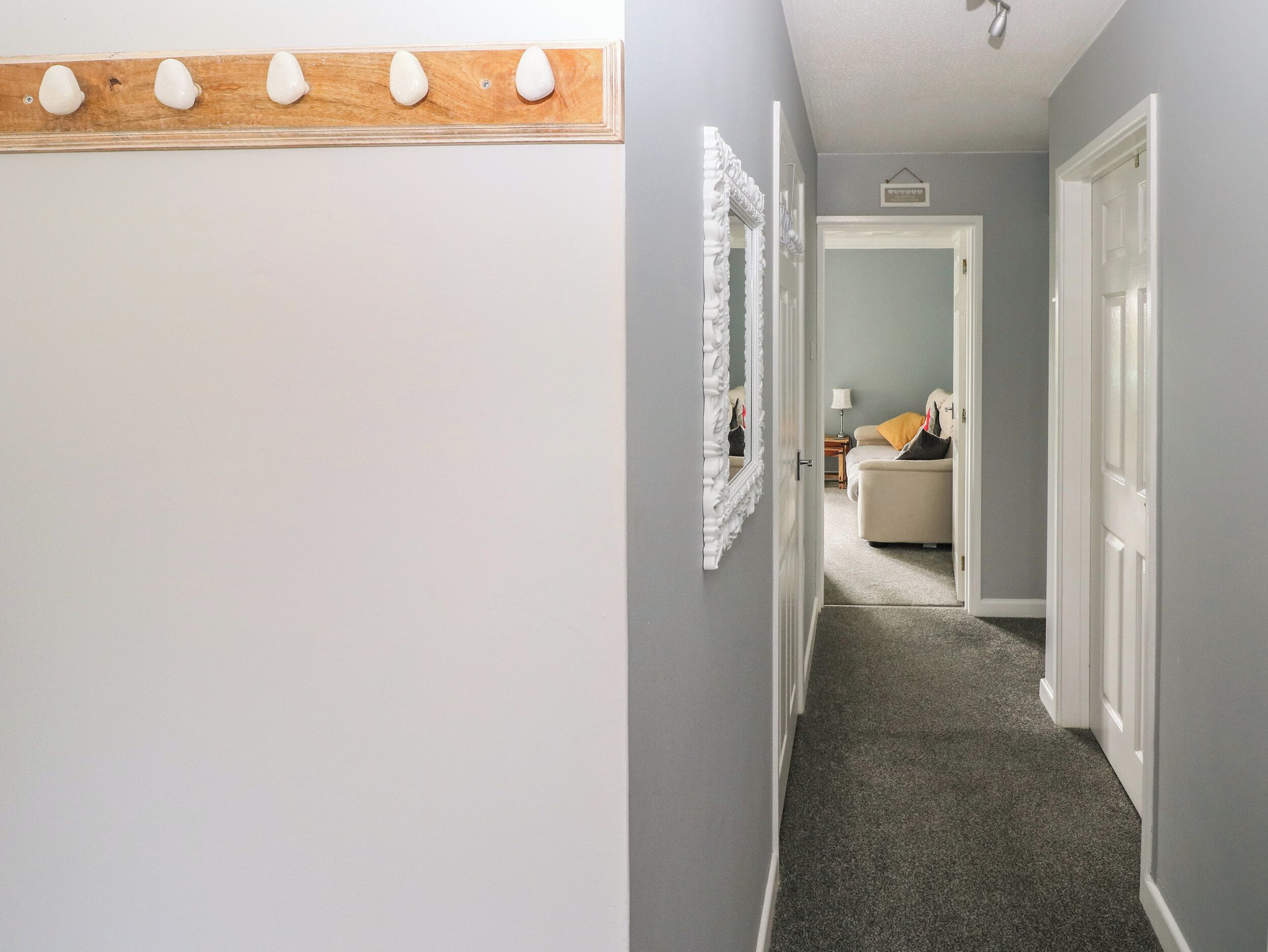 A hallway with a wooden coat rack, a mirror, and a door leading to a room with a bed and a nightstand.