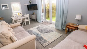 A modern living room with a sofa, a coffee table, a TV, and a dining area with a table and chairs. - Clicketts Court (Tenby)